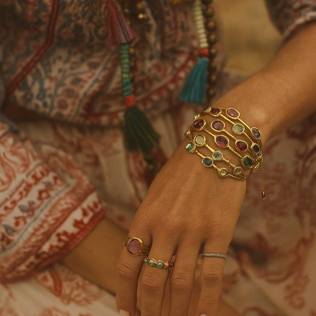 Close-up of a hand wearing colorful jewelry with a patterned garment in the background